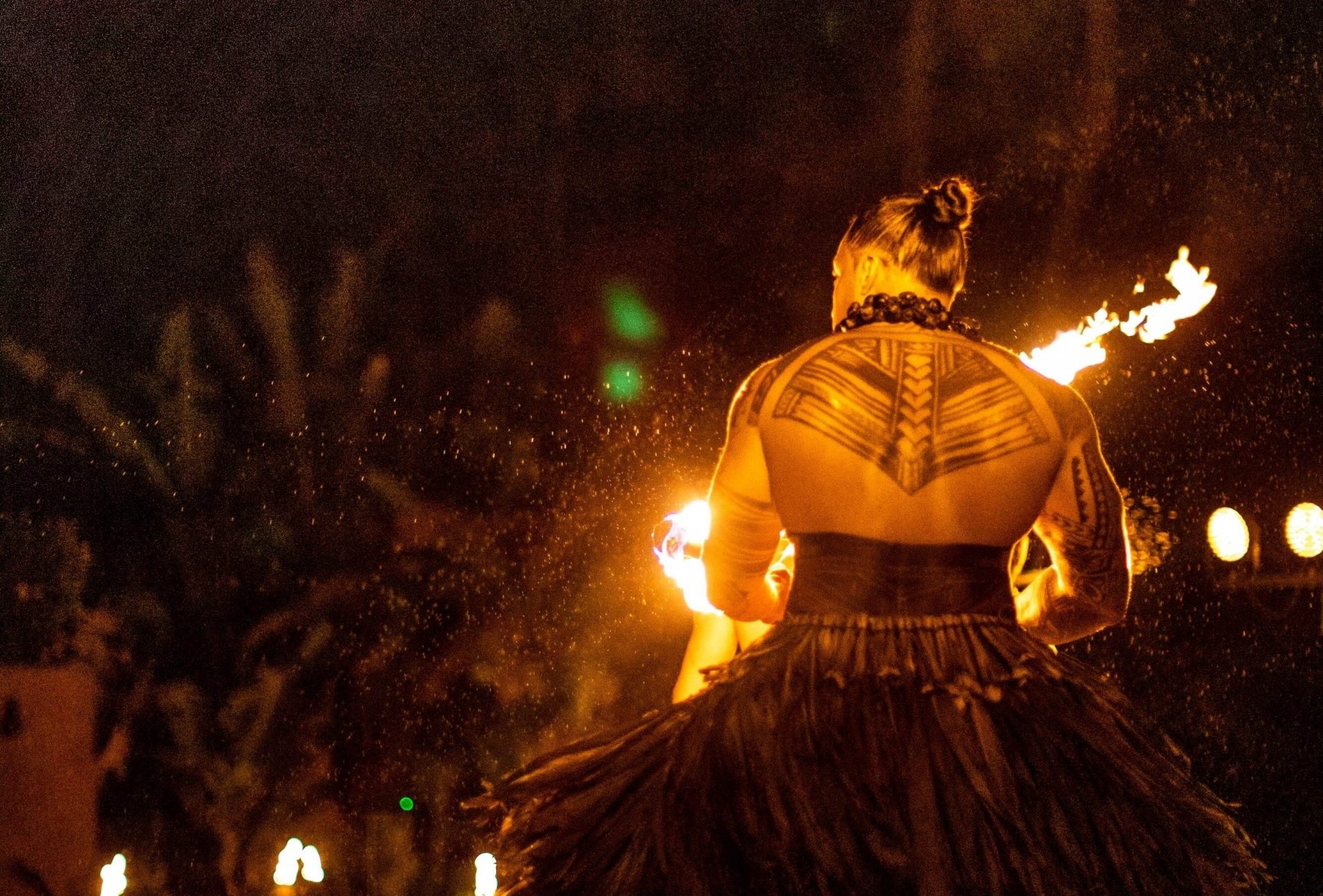 fire performer stands with his back to the camera with large tattoo on his upper back