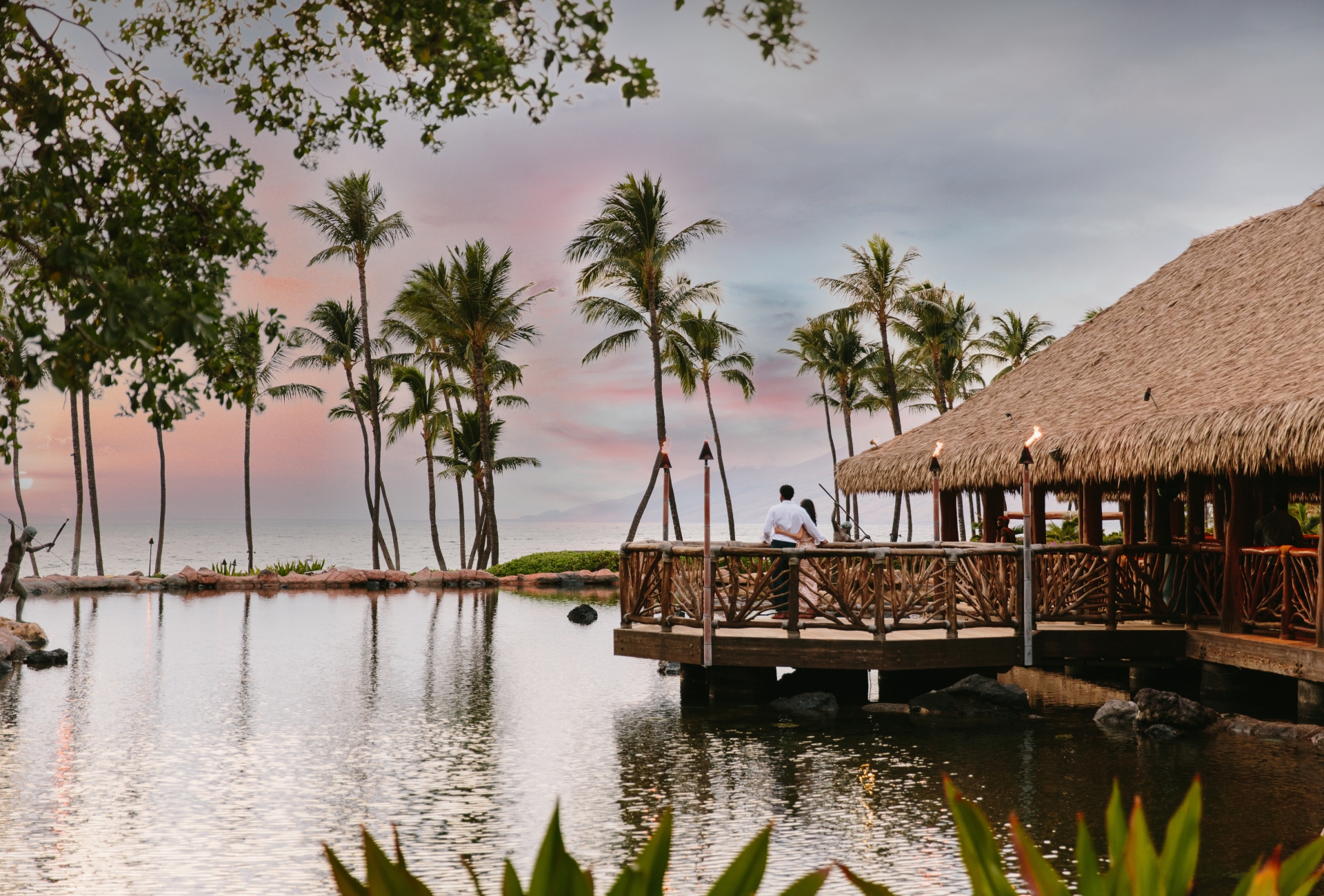 a wooden building overlooks the water lined with palm trees