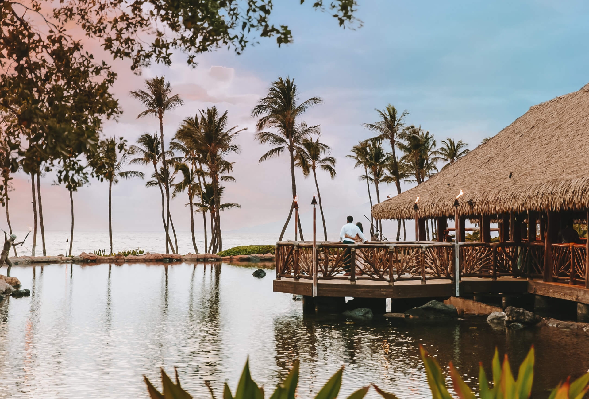 a wooden building overlooks the water lined with palm trees