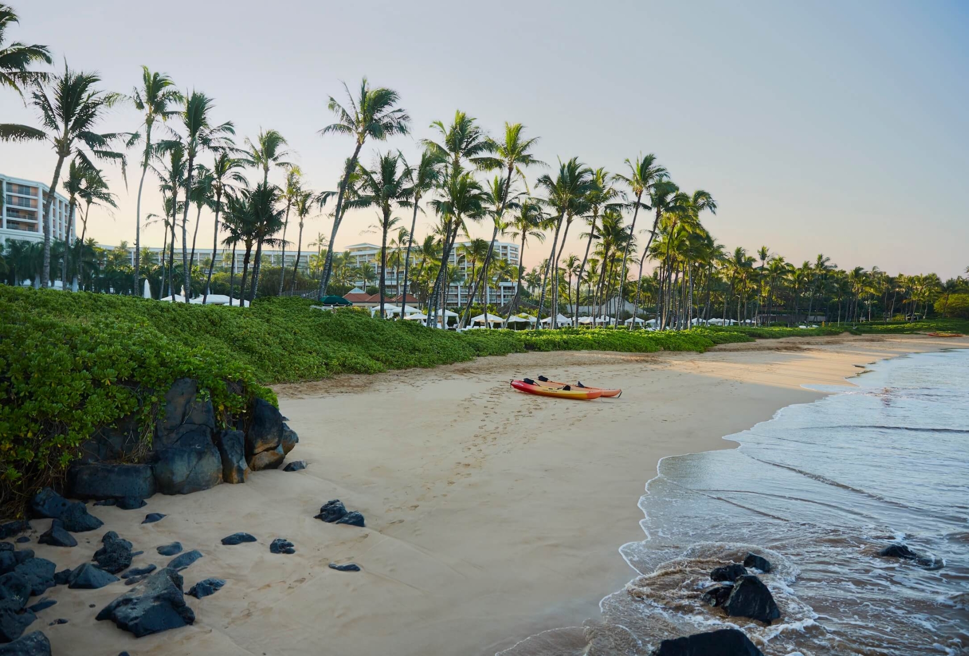 a kayak sits on an empty beach with waves on the sand and palm trees in the background