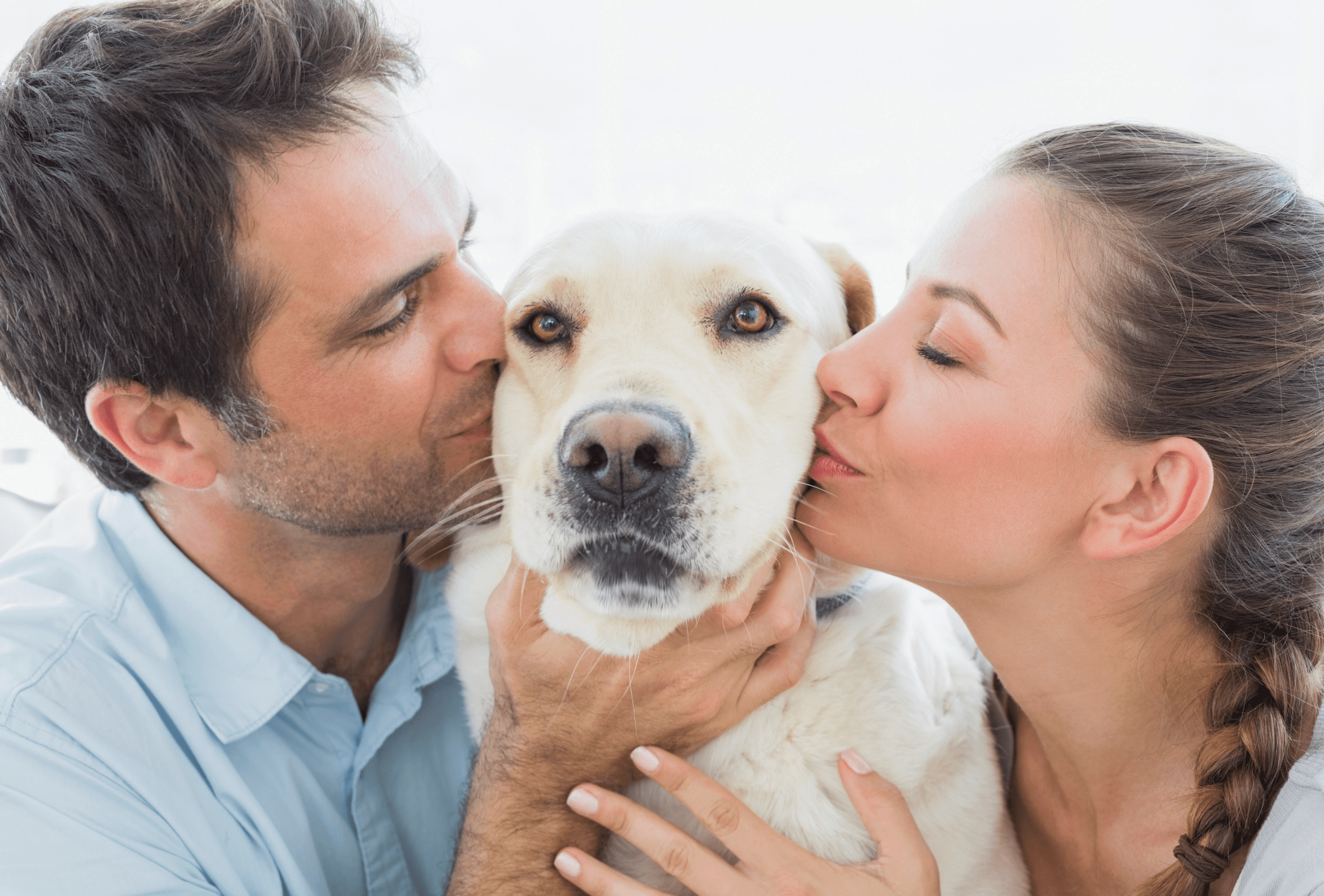 two people kiss both sides of a white dog's head