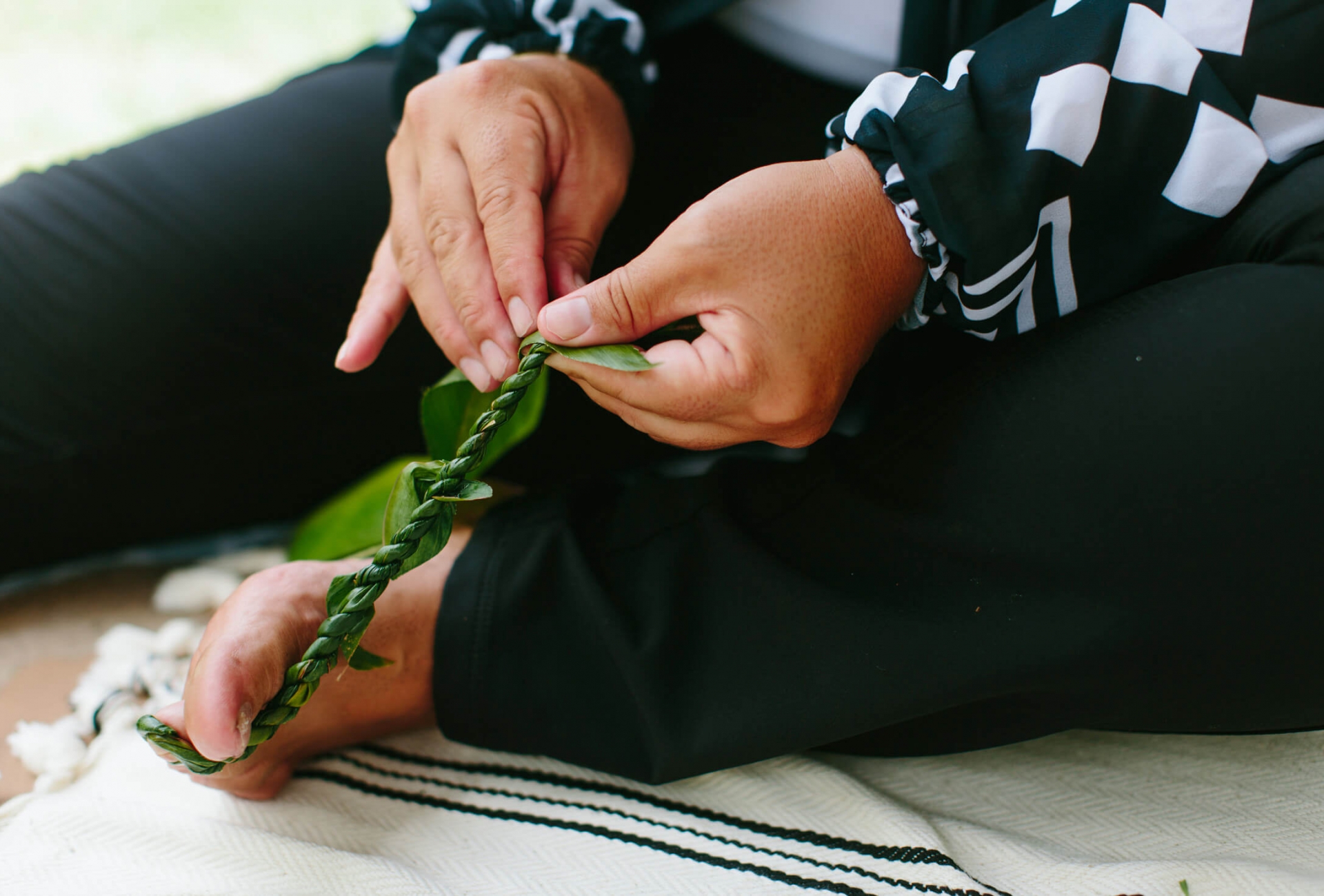 a person weaves a leaf with their hands while holding the base of the weaving with their foot