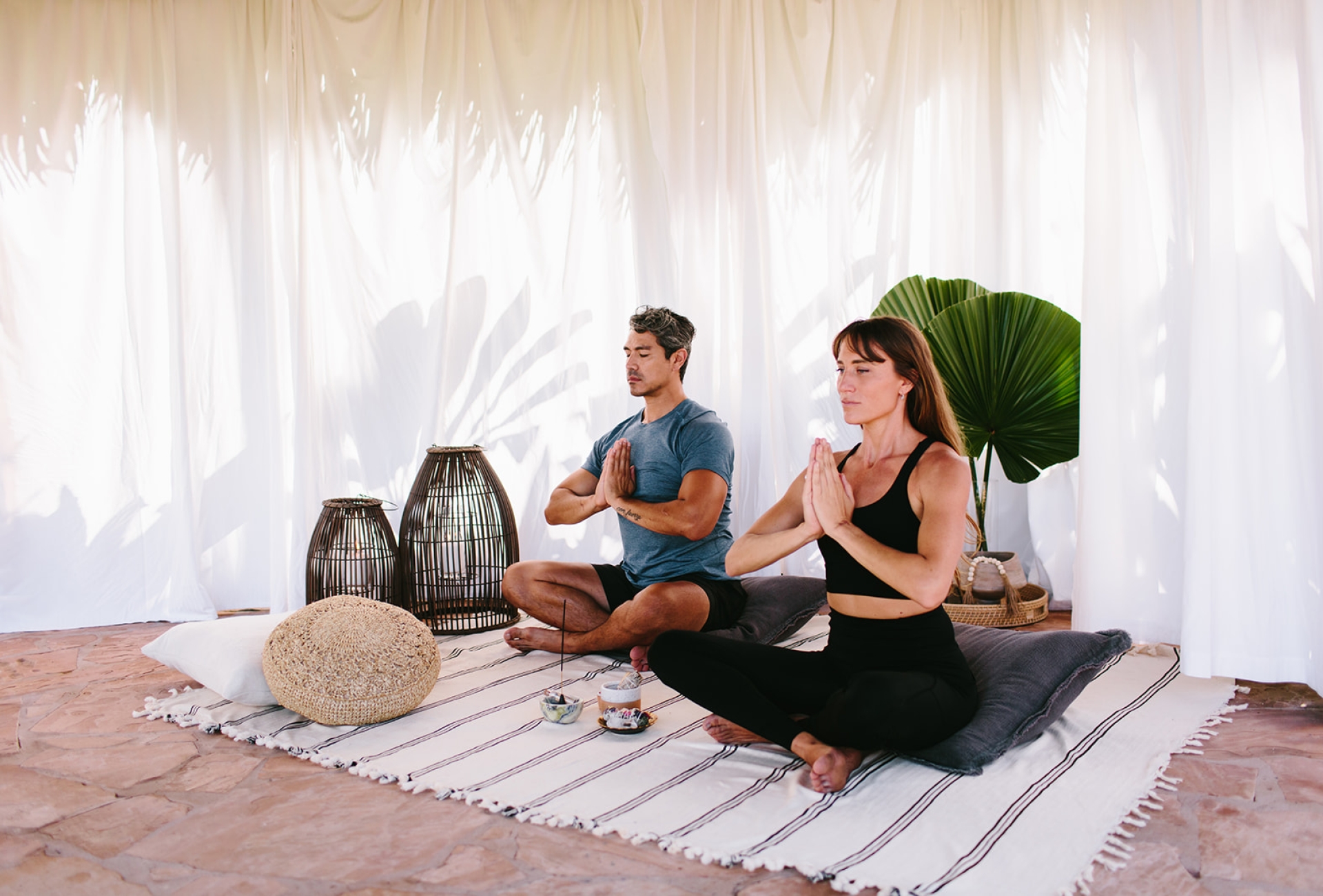 two people sit crosslegged on a striped blanket while meditating