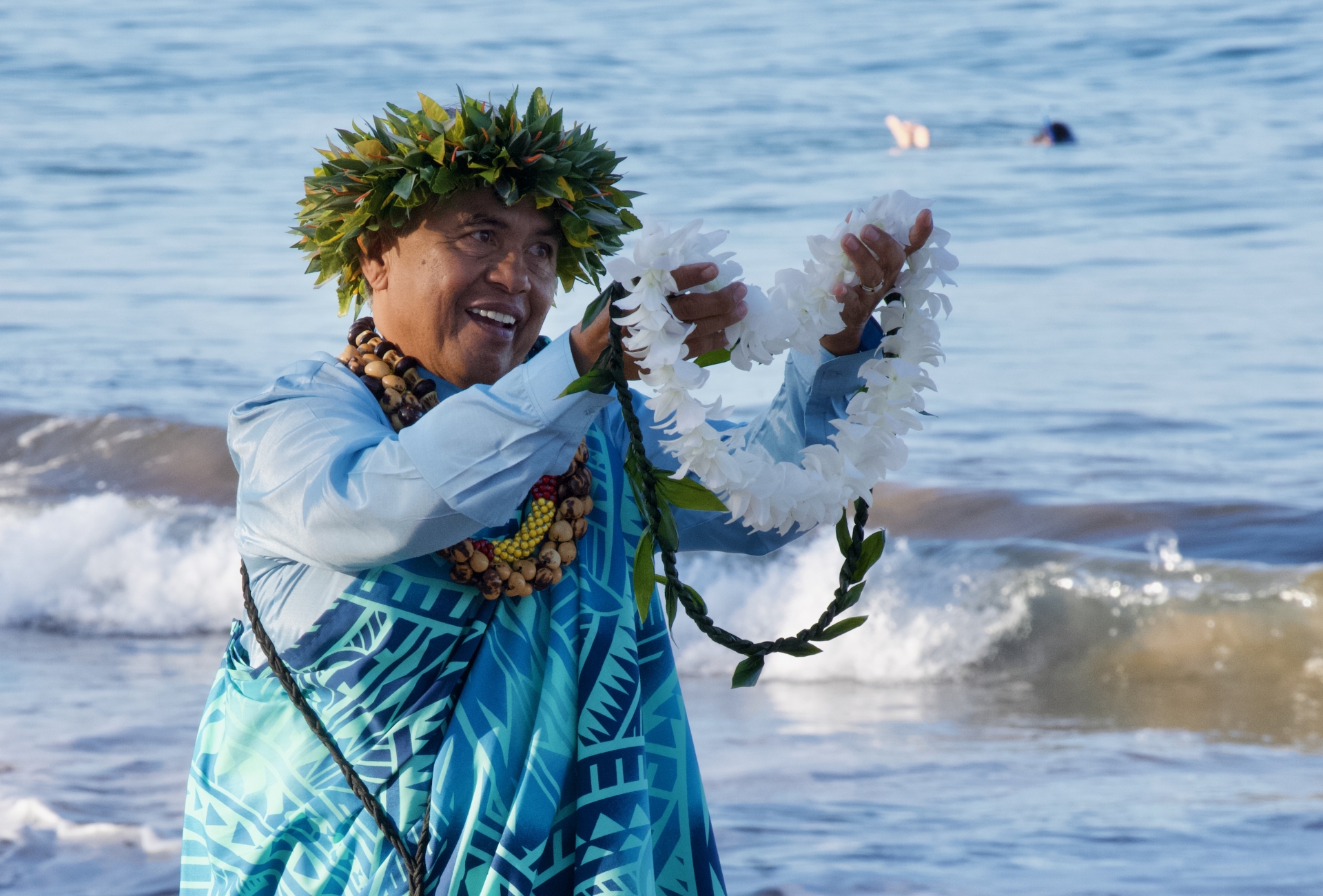 A Hawaiian man on a beach holding out a lei