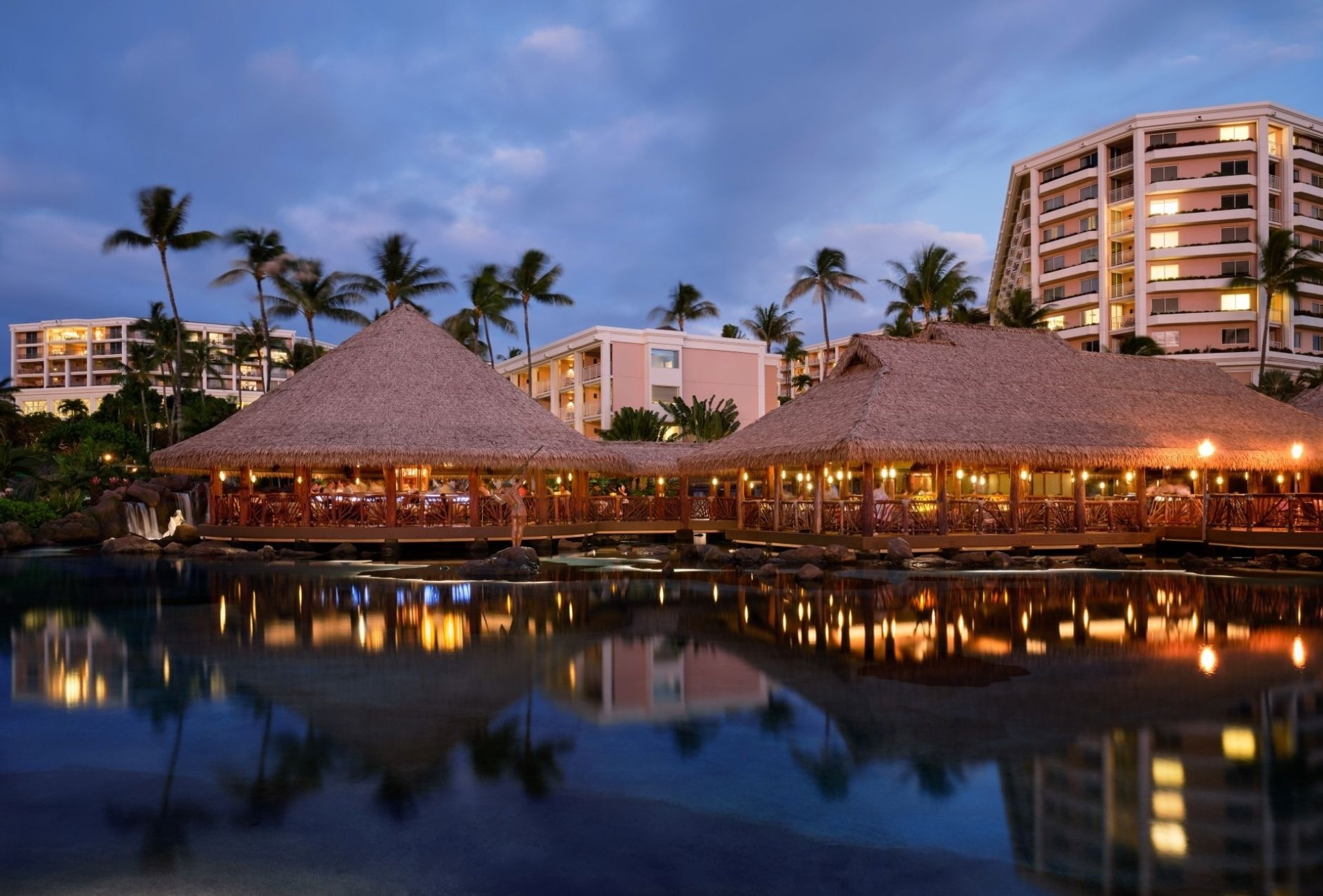 The exterior of Humuhumunukunukuapuaa restaurant - an oceanfront thatched roof building illuminated by lanterns