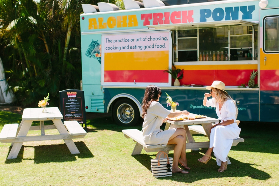 two people sit at a picnic table in front of the Aloha Trick Pony food truck