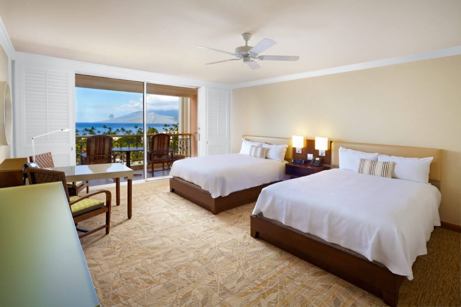 two Queen beds and seating area in Queen Oceanview room with patio doors give view of outside