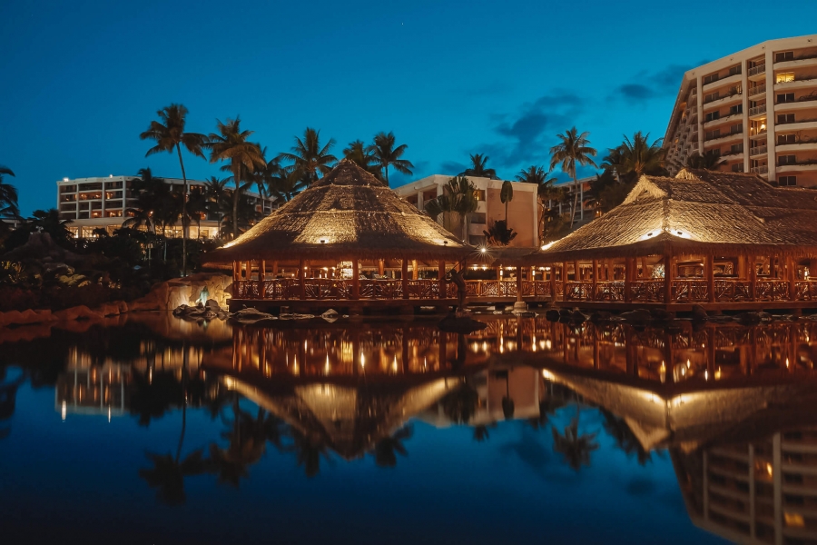 well-lit huts at Grand Wailea restaurant are reflected on the water 
