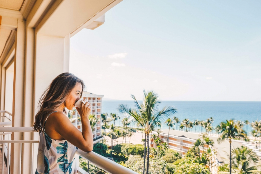 a woman sips her drink while looking off the balcony to the ocean