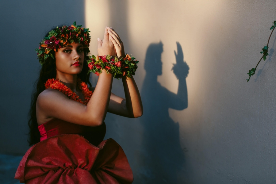 a woman dressed in red dances the luau as the light casts her shadow against the wall beside her