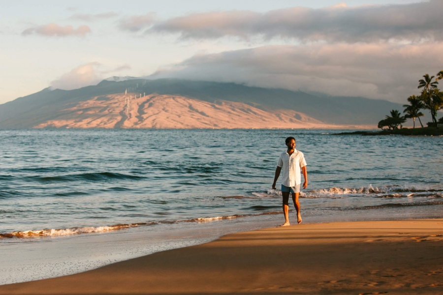 a person walks along the beach beside the ocean with mountains in the background