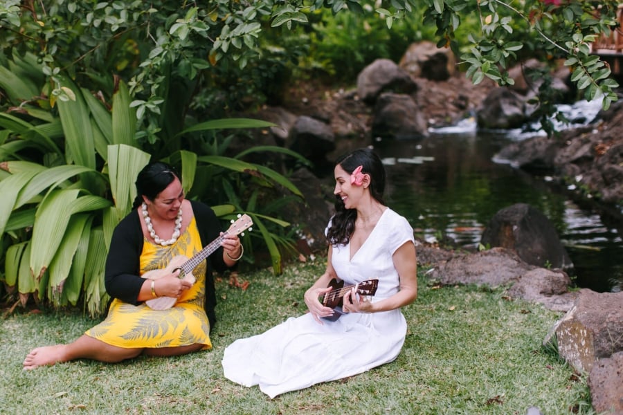 two women sit in the grass while strumming on ukuleles 