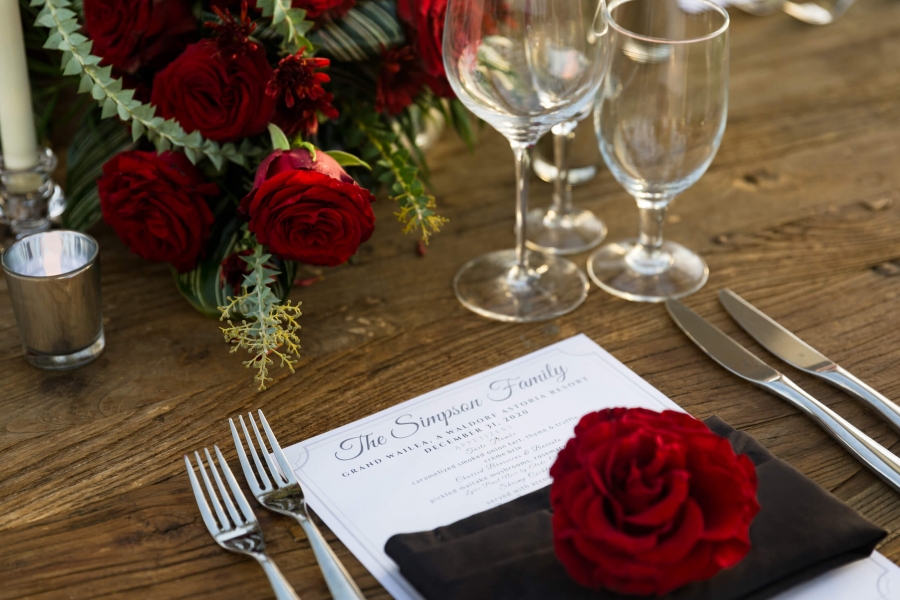 close up of a table setting with empty glassware and red flowers sit on wooden table