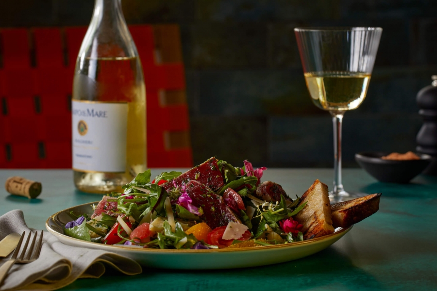 glass of wine with bottle sits behind plate of salad